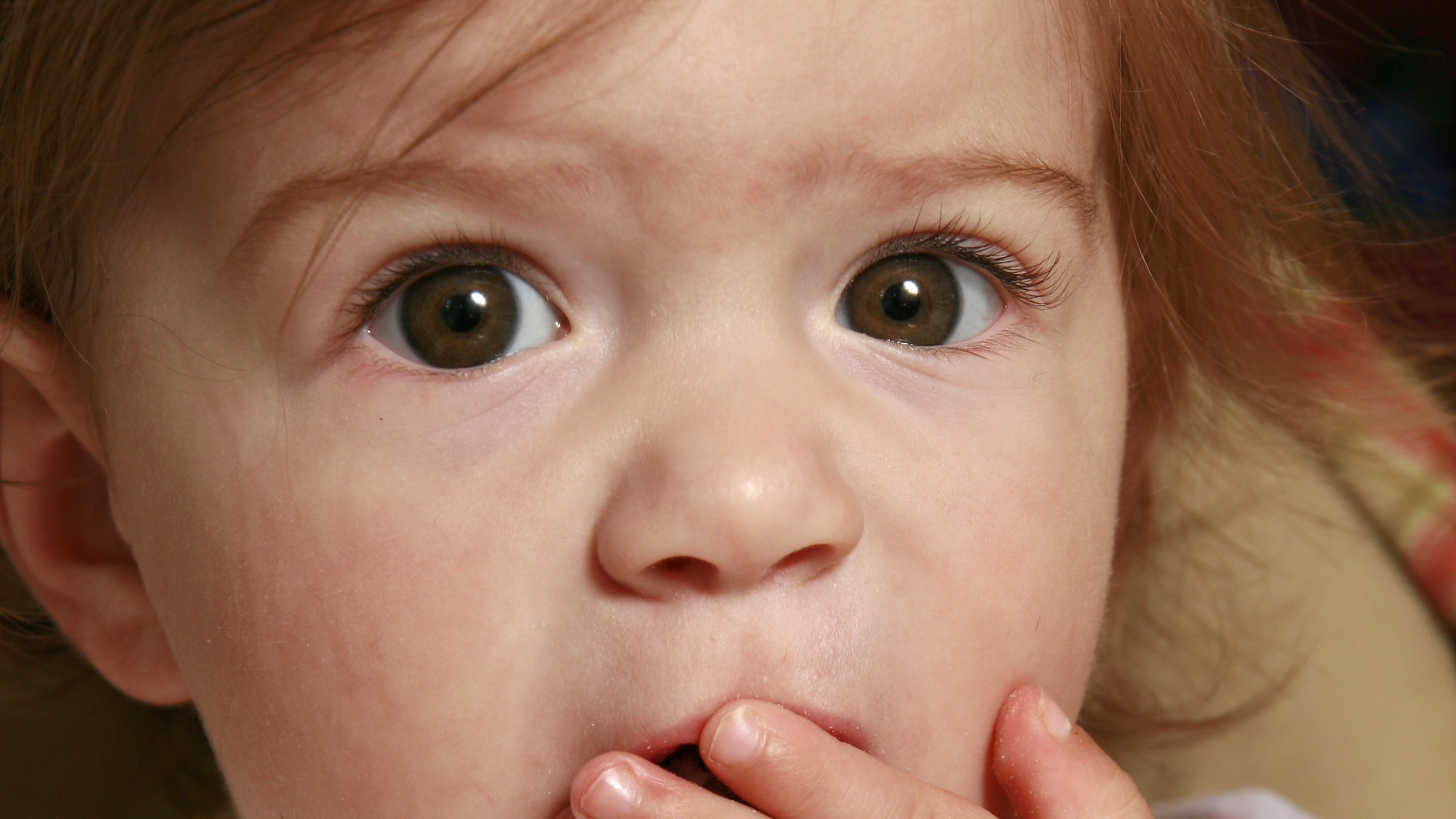 surprised looking wide-eyed baby covering their mouth with their hand