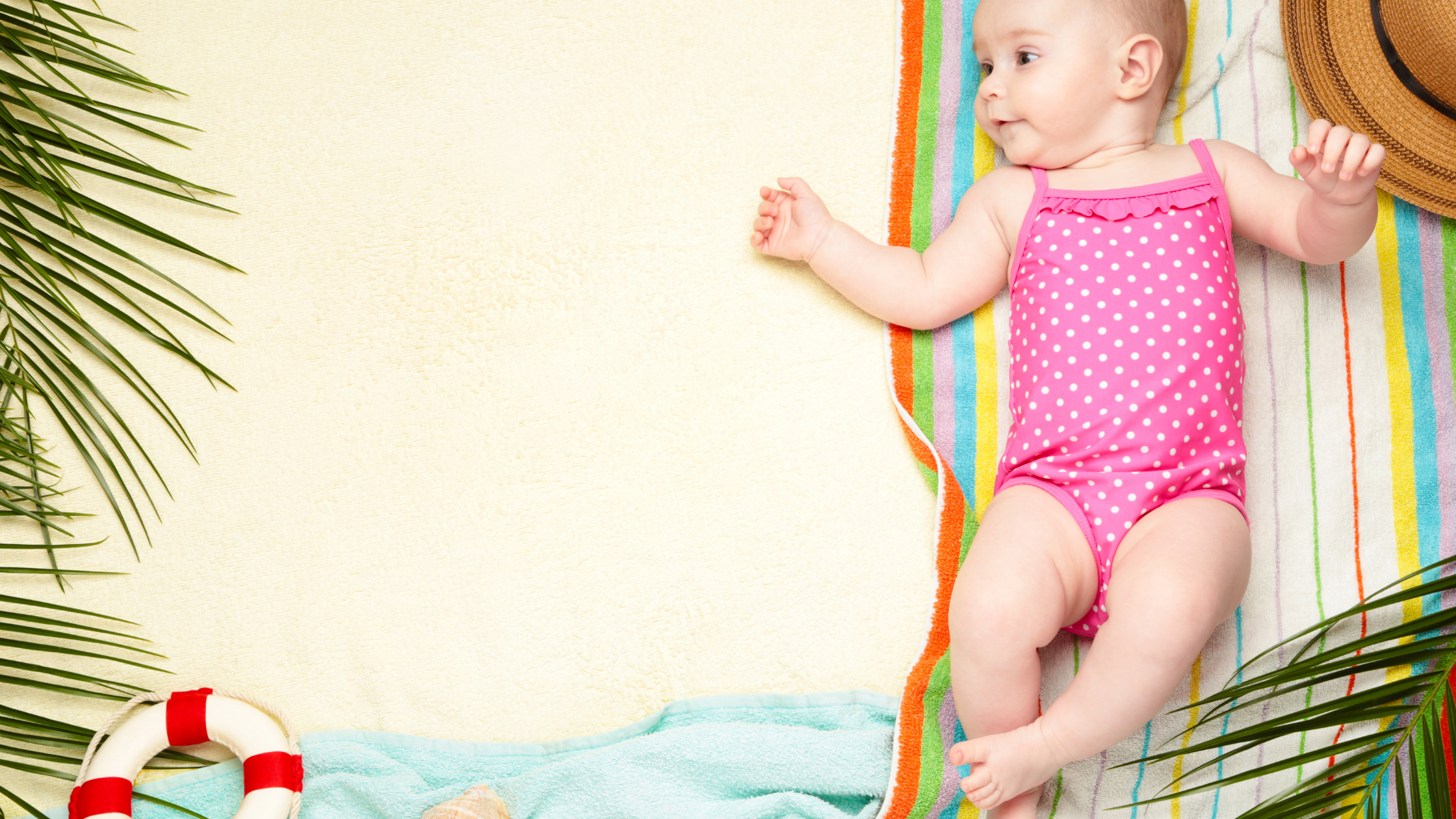 Baby in a pink bathing suit laying on a beach blanket