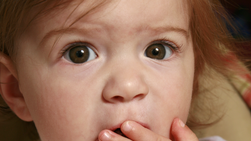 surprised looking wide-eyed baby covering their mouth with their hand
